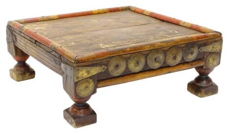 An African tribal low table or stand, decorated with a band part in red with a planked top, faceted brass embellishments and corners on turn supports, in the manner of Bugatti, 53cm wide.