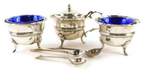 A George V silver three piece cruet, comprising mustard pot and lid and a pair of salts, each with a blue glass liner, and three associated spoons, weighable silver 3¾oz.