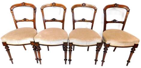 A set of four Victorian walnut balloon back dining chairs, each with a shell carved back, a padded seat on turned tapering legs.