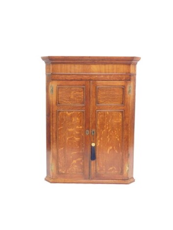 A George III oak and mahogany wall hanging corner cupboard, with two doors opening to reveal three shelves, with key, 109.5cm high, 84cm wide, 48cm deep.