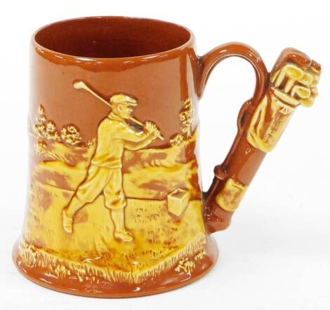 A 20thC Dartmouth pottery golfing tankard, with golf bag handle, the body depicting raised golfing scene, printed mark to base, 14cm high.