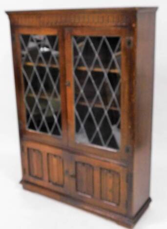 A 20thC oak glazed bookcase, with carved frieze above an astragal glazed door and a pair of linen fold cupboards beneath, on plinth base, 137cm high, 98cm wide, 32cm deep.