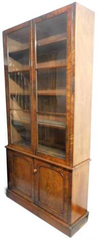 A Victorian mahogany library bookcase, the two glazed doors, raised above two arched cupboards on a block base, 230cm high, 115cm wide, 40cm deep.