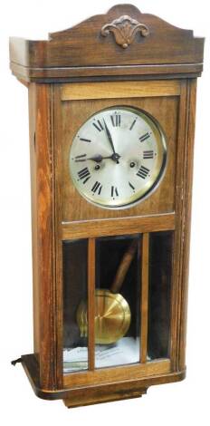 A 1920's oak cased wall clock, with scroll carved plinth top, silvered coloured dial with Roman numerals, pendulum, glazed lower case, 73cm high.