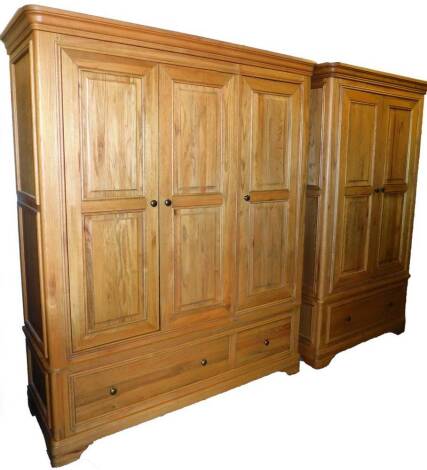 An American light oak two piece bedroom suite, comprising three door and two door wardrobes, each with a moulded cornice, panelled doors and draw beneath on bracket feet, triple wardrobe, 196cm high, 160cm wide, 60cm deep. (2)