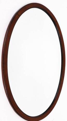 A late 19thC mahogany oval wall mirror, with marquetry chequered banding, 89cm x 58cm.