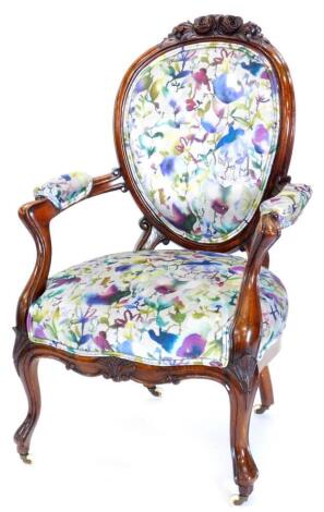 A Victorian walnut showframe armchair, carved with flowers leaves etc., upholstered in vivid floral fabric, on cabriole legs.