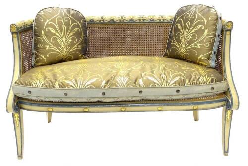 A Regency bergere sofa, painted in cream and powder blue, the frame carved with acanthus, fans and scrolls, with a caned back and seat, fitted gold, blue and black fabric seat cushion with other matching cushions, on sabre legs, 132cm wide.