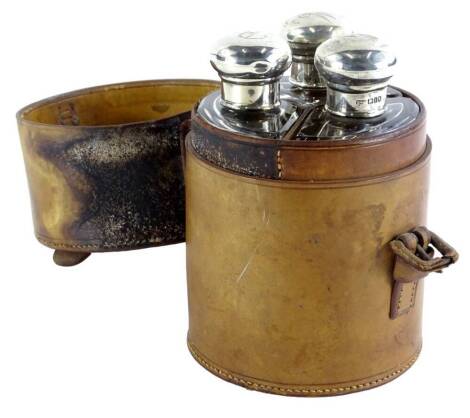 A George V silver three piece glass and silver mounted hunting flask set, in a leather container, strap (AF), each lid engraved with an initial J. R. M., London 1924. bottles 13cm high, 14.5cm high overall, 10cm diameter