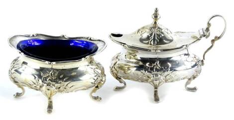 An Edwardian oval silver salt, decorated with shells, scrolls, etc., on four feet, with blue glass liner, and a matching mustard pot, mustard pot lid and one liner (AF), London 1906, 4¼oz.