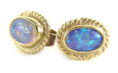 A pair of 9ct gold opal earrings, each set with oval opal in rub over setting, with rope twist borders, single pin backs, with butterfly backs, 1.3g all in.