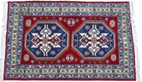 A Turkish type rug, with a design of two large latch hook medallions in mainly blue, maroon and cream, on a red ground with three borders, 237cm x 150cm.