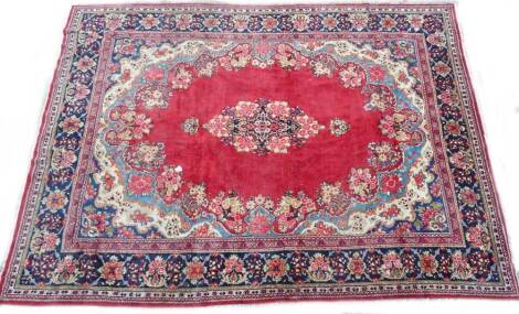 An Eastern carpet, with a central floral medallion, on a red ground with multi-coloured spandrels, one wide and various narrow borders 400cm x 297cm. Label for Nomadic Rugs on the reverse.