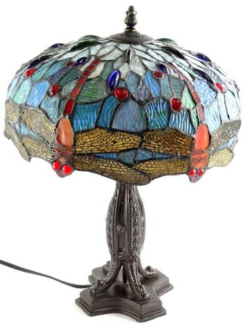 A Tiffany style lamp, the shade decorated with glass cabochon dragonflies etc., the bronzed base with a bullet shaped column, three scroll cast feet and concave platform, 42cm high, shade 32cm diameter.