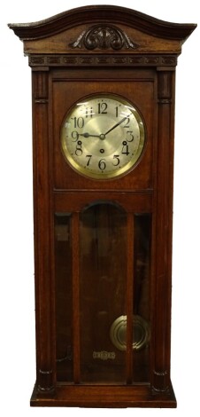 A 1920s mahogany wall clock, with a shaped cornice above a silvered dial and a glazed door, eight day chiming movement.