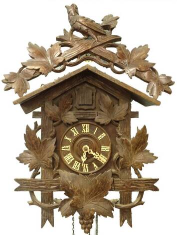 An early 20thC Black Forest cuckoo clock, with a leaf and bird carved crest, the dial applied with ivorine Roman numerals etc., with two weights and a pendulum, 62cm high.