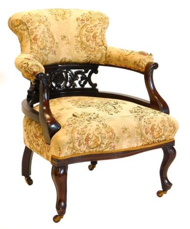 An early 20thC mahogany tub shaped chair, upholstered in tapestry style fabric to the back and seat, on cabriole legs with castors.