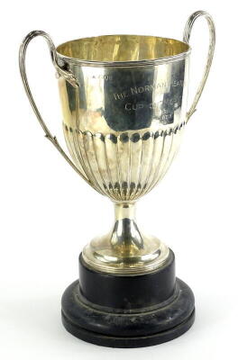 A late Victorian silver two handled trophy cup, with part fluted decoration and tapering foot, engraved the Norman Heaton Cup of merit Won by E M Weir 1939, London 1895, 24¼oz on an ebonised base, 36cm high.