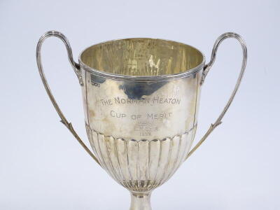 A late Victorian silver two handled trophy cup, with part fluted decoration and tapering foot, engraved the Norman Heaton Cup of merit Won by E M Weir 1939, London 1895, 24¼oz on an ebonised base, 36cm high. - 2