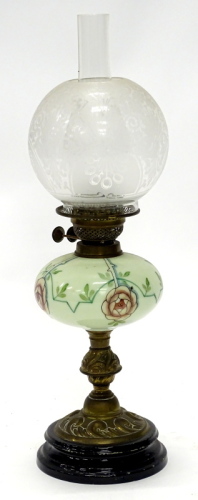 A brass oil lamp, with a clear and frosted globular shade, the green opaque glass reservoir painted with flowers, leaves, etc., on a leaf and scroll cast column and ceramic base, 60cm high.