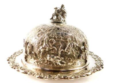 A George IV silver muffin dish and cover, the domed cover with a finial of a seated man with dog, smoking a pipe and holding a mug of ale, chased with figures from the crusades, embossed and engraved with trees and homesteads, the dish with a floral and f