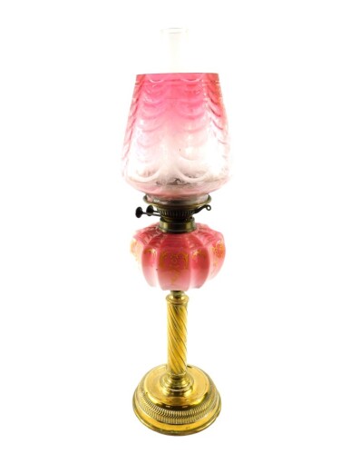 A Victorian brass oil lamp, with an enamel decorated Burmese glass reservoir, glass chimney and floral etched clear to cranberry glass shade, 66cm high.