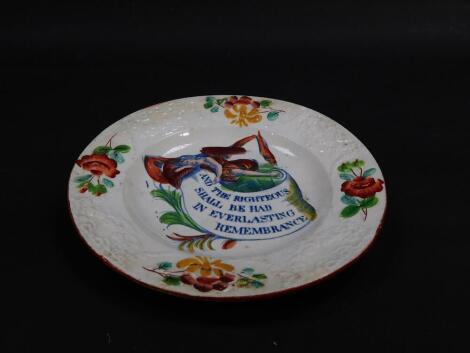 An early 19thC pearl ware commemorative tea plate, clobbered and transfer decorated in blue and white, with an angel and scroll "and the righteous shall be had in ever lasting remembrance" within a moulded border of floral swags, roses and other flowers, 