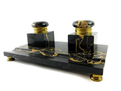 A French late 19thC veined black marble desk stand, with a pair of square integral inkwells with hinged gilt metal mounted lids, raised on a rectangular base with pen recess, on brass feet, 28cm wide, 17.5cm deep.