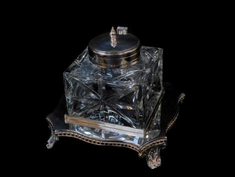 A silver and cut glass inkwell, the inkwell with plated mount and hinged lid, on a serpentine base with beaded rim, raised on leaf scroll feet, Mappin and Webb, London 1989, base 4.19oz.