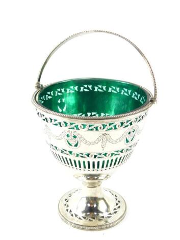 A George III silver sugar basket, with green glass liner, swing handle, pierced and engraved with classical urns, swags and foliate scrolls, oval shield reserve, crest engraved, William Bateman I, London 1820, 5.19oz.