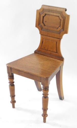 A Victorian oak hall chair, with a carved and scroll back and solid seat, raised on turned legs.