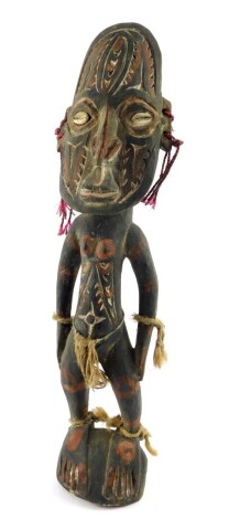 A Papua New Guinea Sepik carved wooden figure, modelled in standing pose, with a mask type head, inset shell eyes, painted all over in traces of red, with carved foliate decoration, 42cm high.