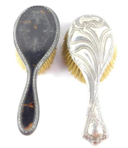 A George V silver and tortoiseshell hair brush, with pique decoration, Birmingham 1910, and a further silver backed hair brush with Art Nouveau scrolled and leaf embossed decoration, Birmingham 1911. (2)