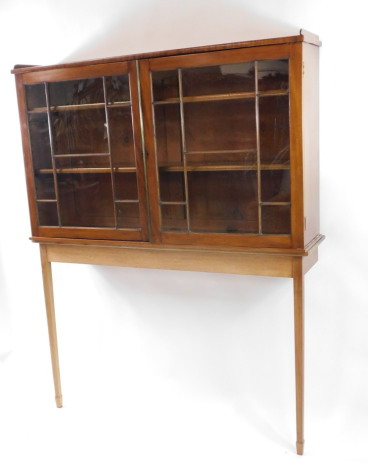 A mahogany display cabinet on stand, with a pair of astragal glazed doors opening to reveal two shelves, on a later teak console table base, raised on tapering square legs and spade feet, 173cm high, 135cm wide, 31.5cm deep.