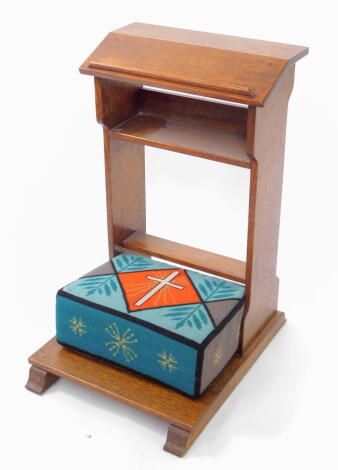 An early 20thC oak church or chapel prayer kneeler, with a single shelf and wool work cushion, 75cm high, 45cm wide, 56cm deep.