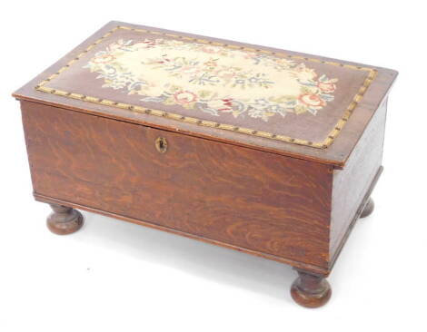 A Victorian oak ottoman, with a floral wool work seat, raised on bun feet, 38cm high, 73cm wide, 43cm deep.