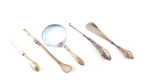 An Edward VII button hook with silver handle, embossed with rococo scrolls, shield reserves, Chester 1907, shoe horn with silver handle, similarly decorated, Chester 1908, paper knife with silver handle, magnifying glass with silver handle and a mate drin