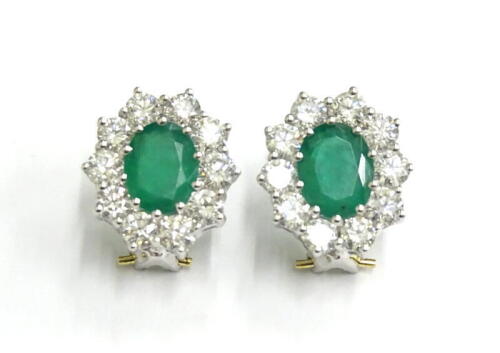 A pair of emerald and diamond cluster earrings, each set with oval emerald and surrounded by round brilliant cut diamonds, emeralds totalling approx 3.6cts, diamonds totalling 3cts, in white gold setting, with yellow gold backings, clip backs, 3.4g all in