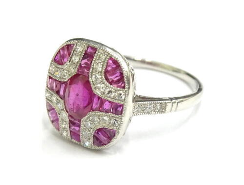 An Art Deco style ruby and diamond ring, set with oval and baguette cut rubies, and round brilliant cut diamonds, with diamond set shoulders, in white metal setting, platinum, ring size N½, 4.1g all in.