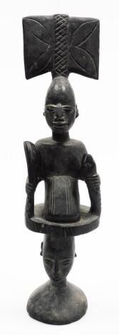 A heavily carved ebonised African tribal totem style figure, formed as two figures with elaborate features on a circular base, 54cm high.