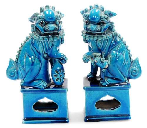 A pair of Chinese turquoise glazed pottery dogs of fo, each on shaped partially pierced bases, unmarked, 23cm high. (2)