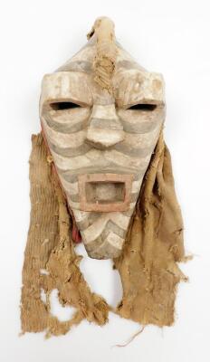 A heavily carved African tribal face mask, in black and white decoration with pierced raised eyes and other heavily carved features, with part cloth surround, 34cm high.