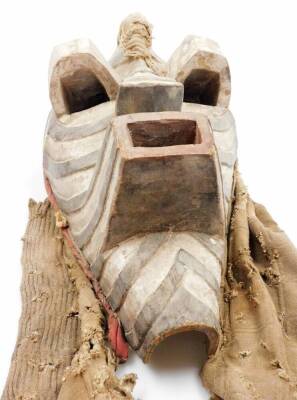 A heavily carved African tribal face mask, in black and white decoration with pierced raised eyes and other heavily carved features, with part cloth surround, 34cm high. - 2