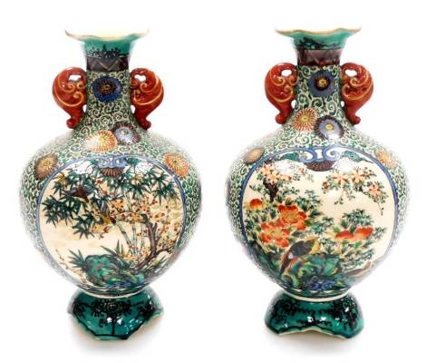 A pair Japanese Kutani pottery bulbous vases with compressed trumpet necks, decorated with panels of flowers within a scrolling karakusa (octopus tentacle) and flowerhead ground, on shaped feet, Meiji period, 29cm high. (2)