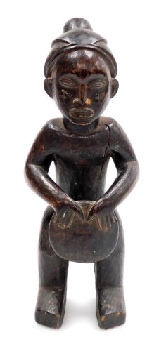 An African tribal carved figure, formed holding drum, with elaborate head dress, 34cm high.