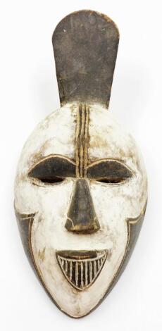 A heavily carved African tribal face mask, with pierced eyes and elaborate mouth, decorated in black and white, 38cm high.