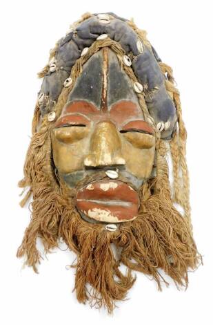 A heavily carved African tribal head, with hair and beard picked out with shells, with pierced eyes, partially painted red and black, main body, 39cm high.