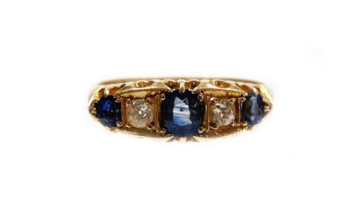 A Victorian 18ct gold sapphire and diamond ring, set with three oval cut sapphires, each in claw setting and two round brilliant cut diamonds, in a boxed Deco type frame surround, with fanned shoulders, ring size O, 4g all in.