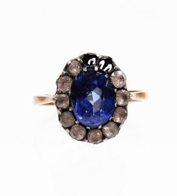 An Edwardian style dress ring, with synthetic sapphire and paste stones arranged in a floral cluster, size M, two white paste stones lacking, on a yellow metal band, unmarked, 3g all in.