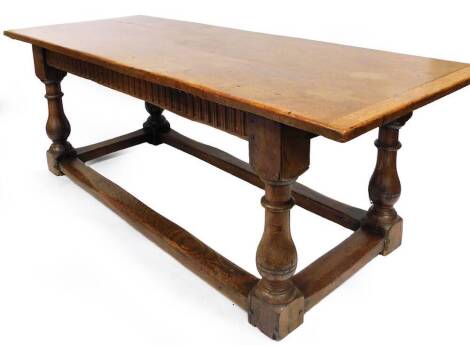 An early 19thC oak refectory table, the plank top with cleated ends, above a carved panel frieze on baluster legs with rectangular supports, 75cm high, 213cm wide, 82cm deep.